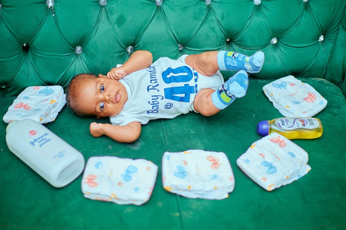 A baby lying on a couch surrounded by nappies and baby care items.