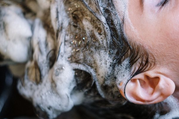A woman enjoying a soothing hair wash with foamy shampoo lather at a salon sink.