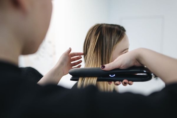 A hairstylist using a straightening iron to smooth a client's hair during a salon hair treatment.
