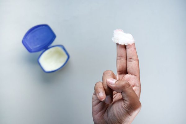 A hand scooping petroleum jelly from an open jar, with jelly visible on the fingers.