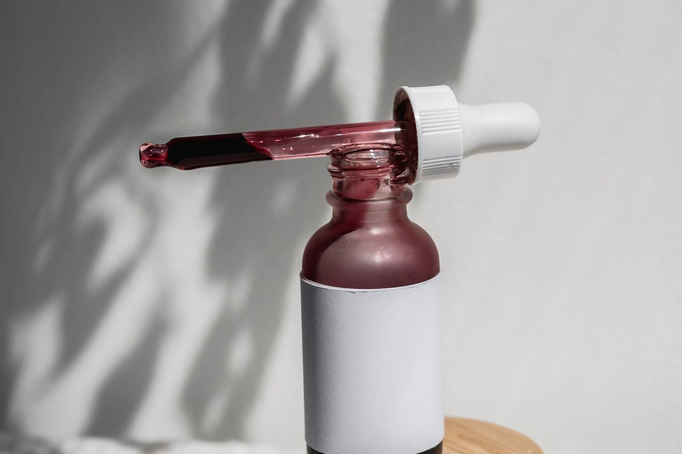 Minimalist still life of a cosmetic serum bottle with a dropper casting artistic shadows.